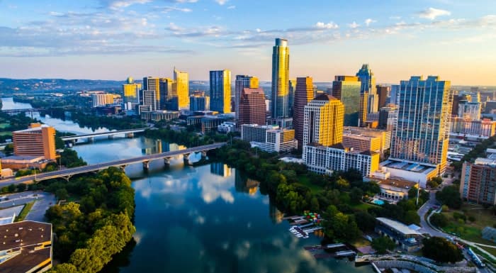 Aerial view of downtown Austin, Texas, showing tall buildings, bridges, and the river reflecting the skyline at sunset—a city often listed among great places to move too.