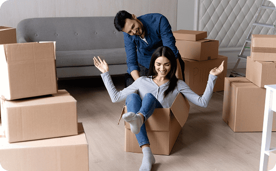 A man pushes a smiling woman sitting in a cardboard box, surrounded by moving boxes in their living room—capturing the joy often echoed in brightside testimonials Trustpilot users share.